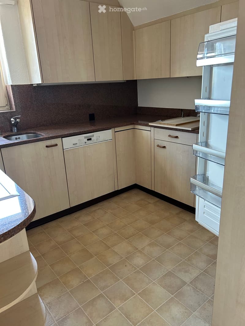 Modern kitchen with light wooden cabinets, tiled floor, and built-in appliances including a refrigerator and dishwasher.