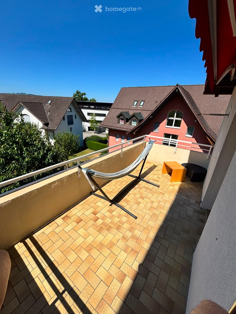 Balcony with wooden decking, metal railing, a hammock, a small table, and a chair.