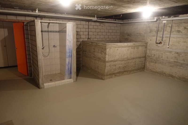 Underground bathroom with a tiled shower stall and a concrete bathtub, exposed pipes, and a concrete floor.