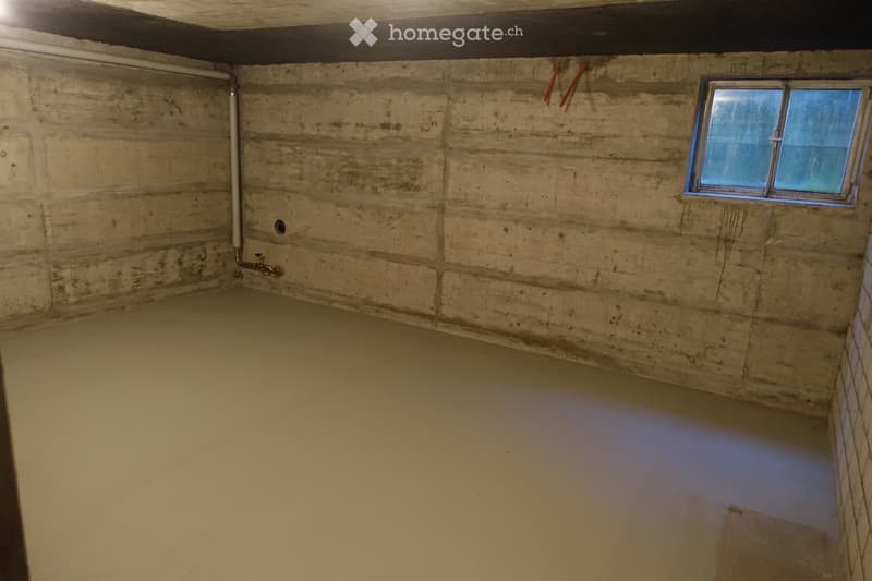 Empty basement room with concrete walls, a small window, and a water pipe with a faucet.