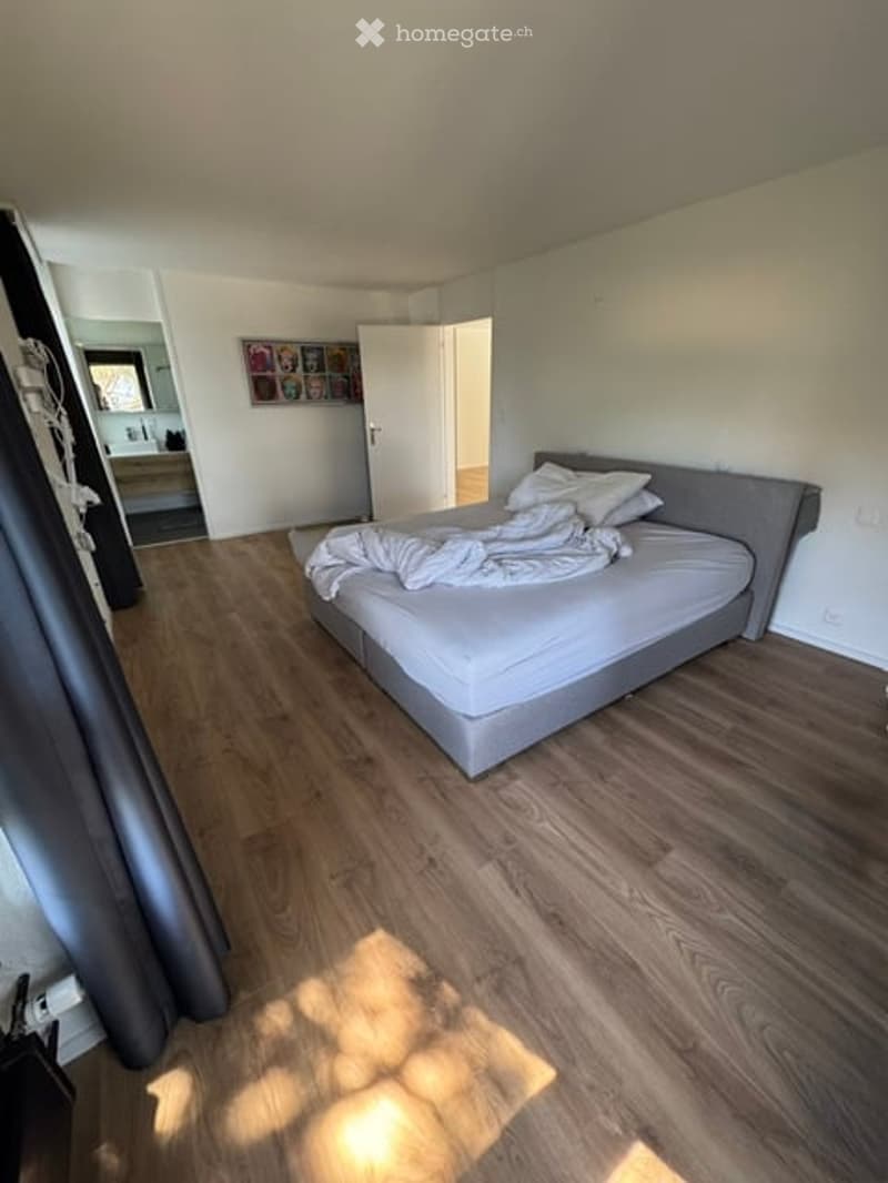 Modern bedroom with a grey bed frame, white bedding, wooden flooring, and a large mirror on the wall.