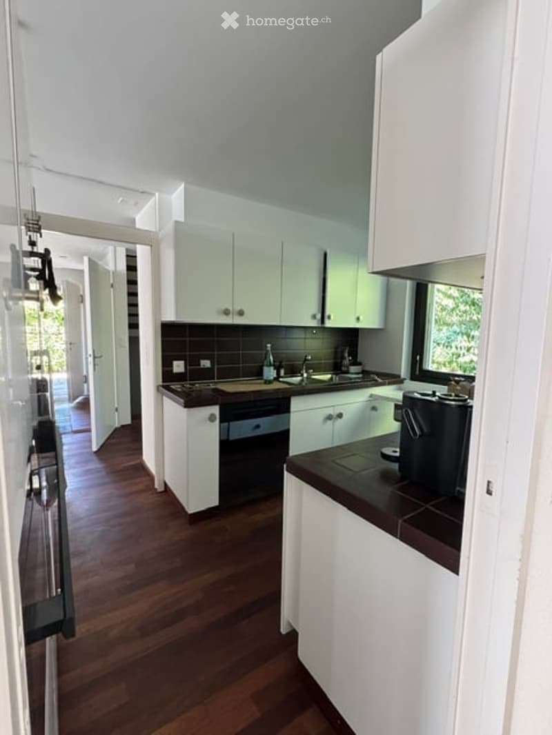 Modern kitchen with white cabinets, dark countertops, and wooden flooring. Features a sink, dishwasher, and coffee maker on the counter.