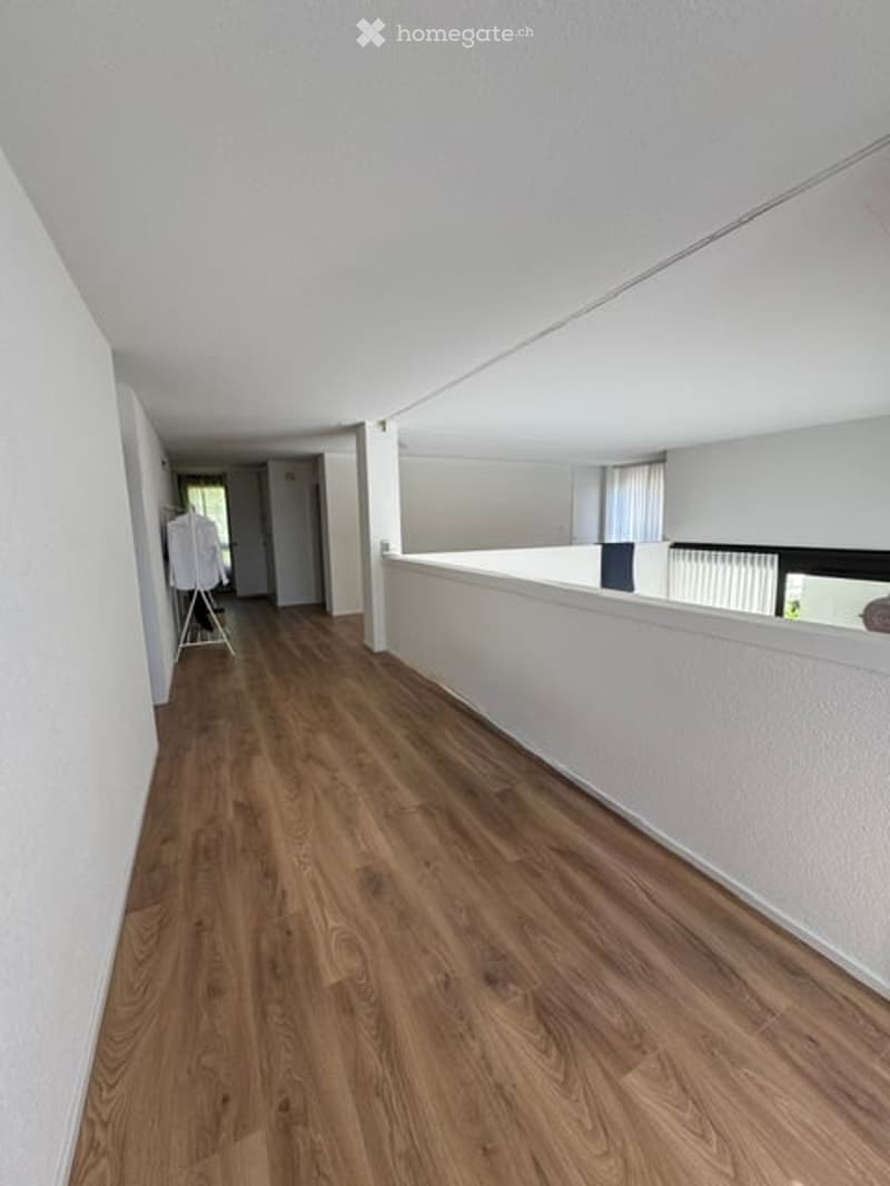 Empty hallway with wooden flooring and white walls, leading to an open area with a white partition.