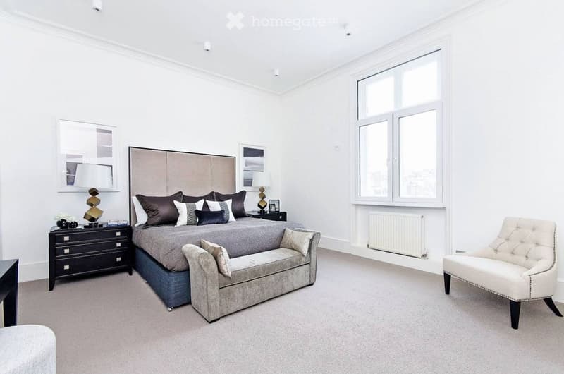 Modern bedroom with a large bed, nightstand, chair, and picture frames on the wall.