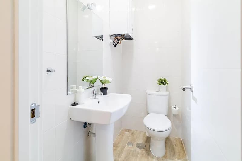 Modern bathroom with white tiles, a sink, toilet, mirror, and small decorative plants.