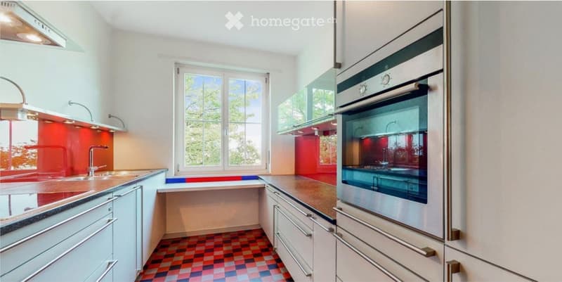 Modern kitchen with white cabinets, stainless steel oven, red backsplash, and a colorful checkered floor.