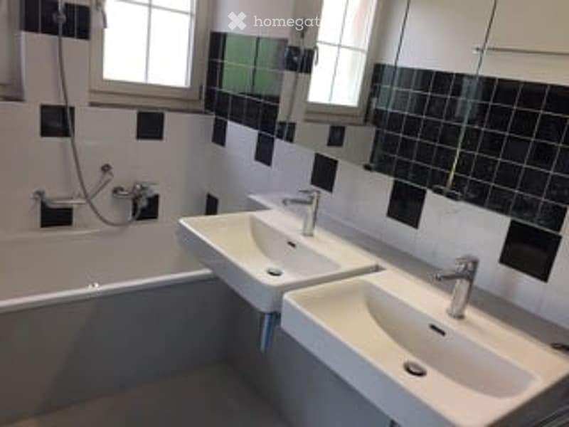Modern bathroom with black and white tiled walls, a bathtub, two sinks, and a large mirror above them.
