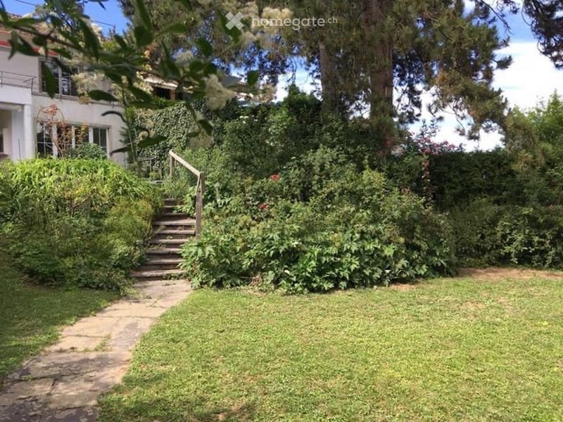 A well-maintained garden with a stone pathway leading to a wooden staircase, surrounded by lush greenery and trees.