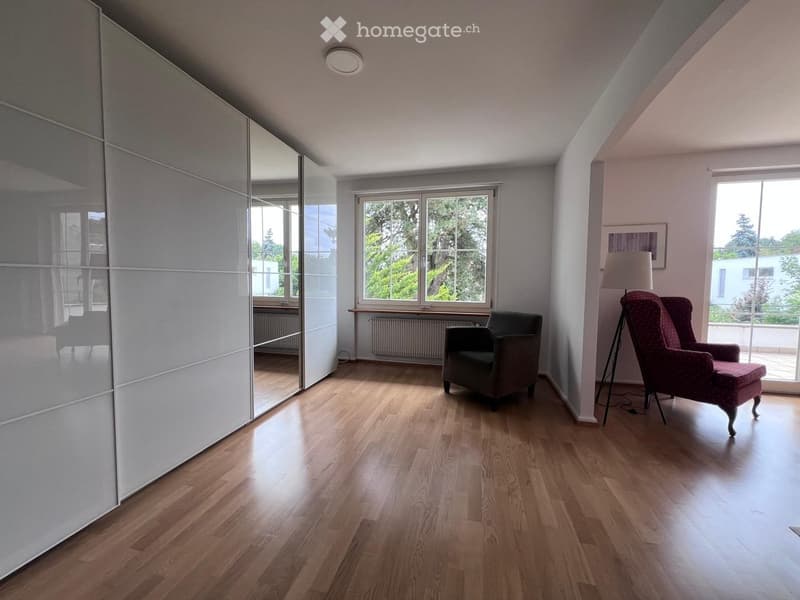 Bright living room with wooden flooring, large windows, two armchairs, a floor lamp, and a large mirrored wardrobe.