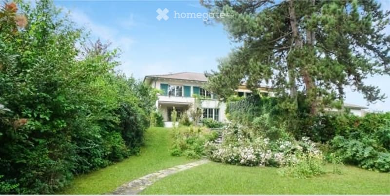 A two-story white house with green shutters, surrounded by lush greenery and a well-maintained garden.