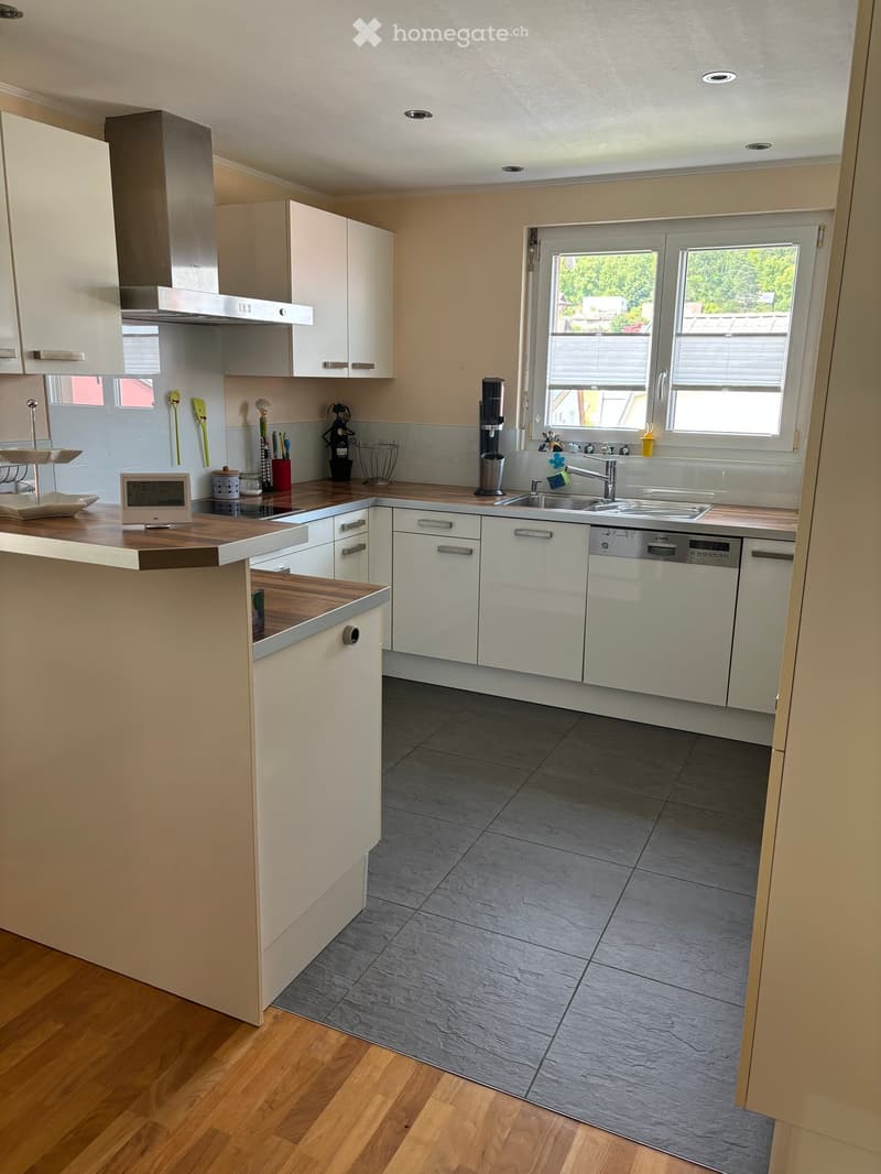 Modern kitchen with white cabinets, wooden countertops, stainless steel appliances, and a central island. Features a sink, dishwasher, and various small appliances.