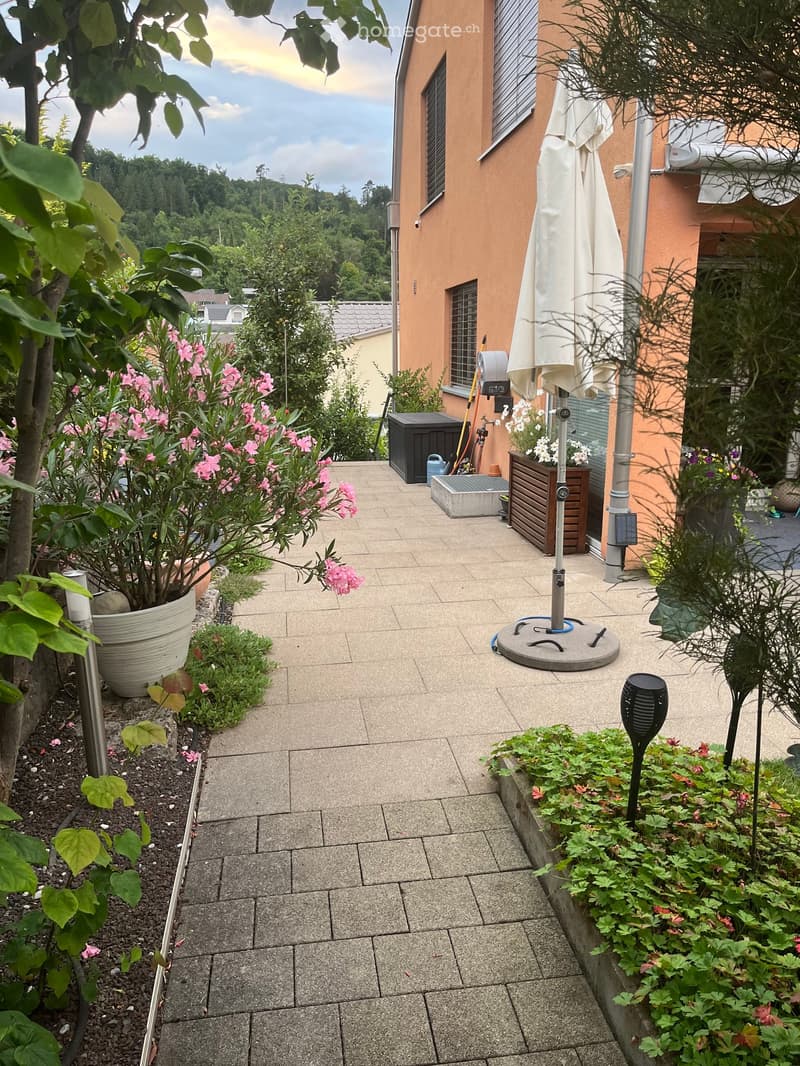 Garden patio with tiled floor, potted plants, umbrella stand, and surrounding greenery.