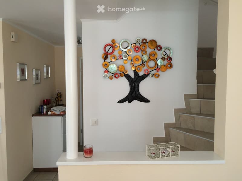 Hallway with a decorative metal tree wall art, a small table with a candle and a decorative basket, and a staircase leading upwards.