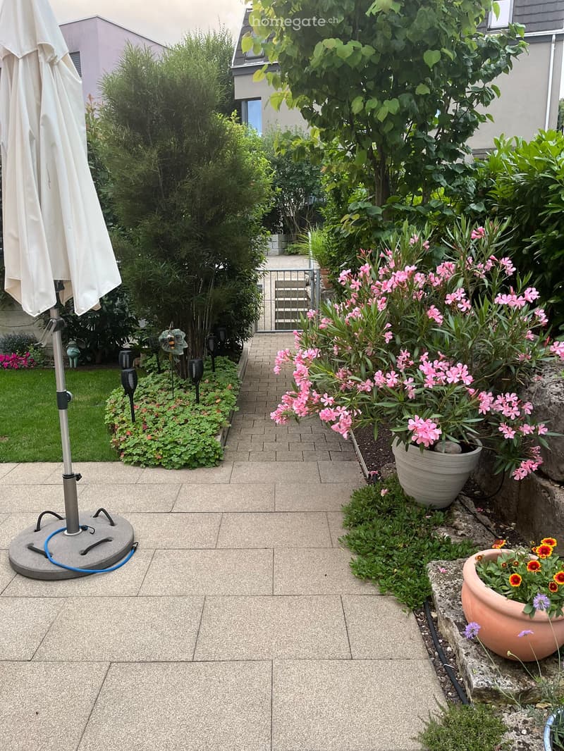 Well-maintained garden with potted plants, flowers, and a patio area with a large umbrella stand.