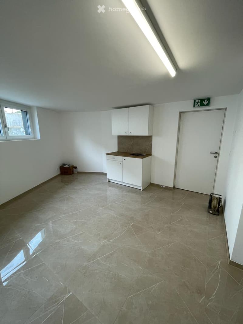 Empty room with white walls, tiled floor, small window, white cabinet, and a door.