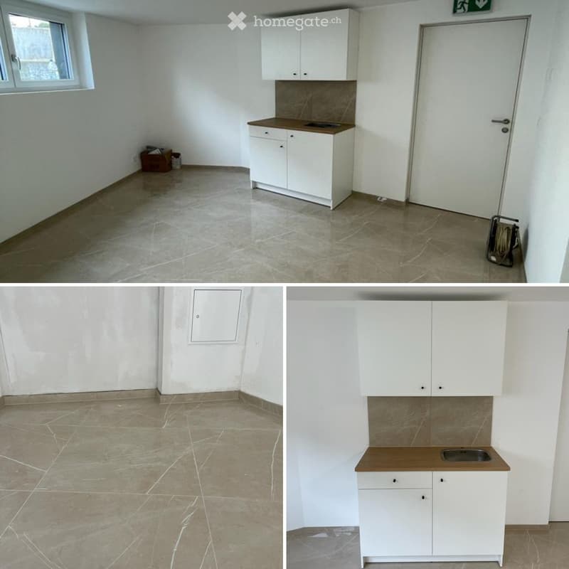 Empty room with white walls, tiled floor, and a small kitchen area with white cabinets and a countertop.