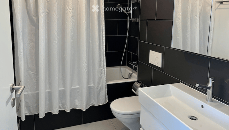 Modern bathroom with black tiled walls, white bathtub, toilet, sink, and shower curtain.