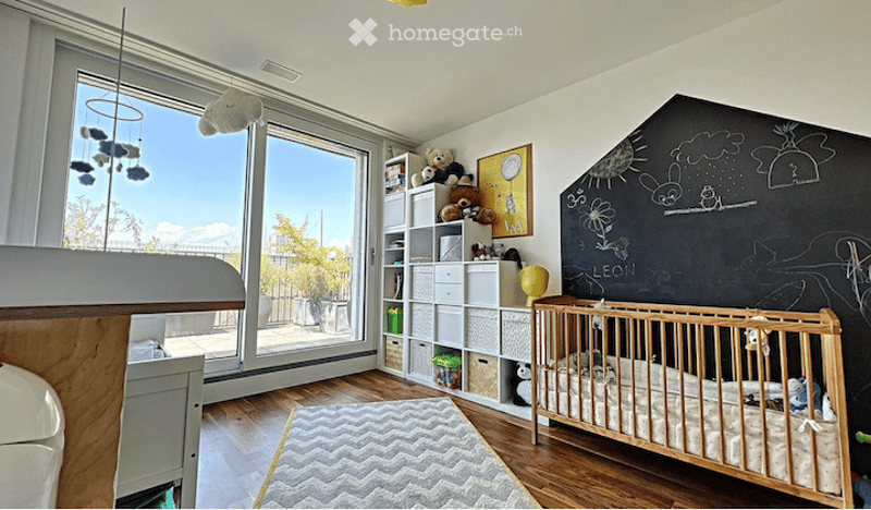 Bright, modern children's bedroom with large windows, a crib, shelves filled with toys, a rug, and a chalkboard wall with drawings.