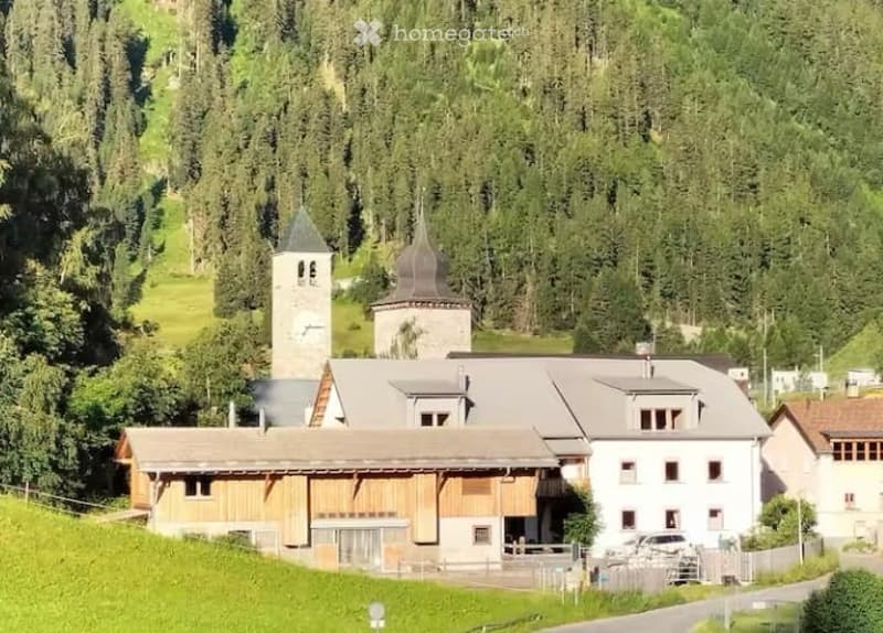 A large, multi-building complex with a mix of wooden and stone structures, surrounded by lush green forest and hills.