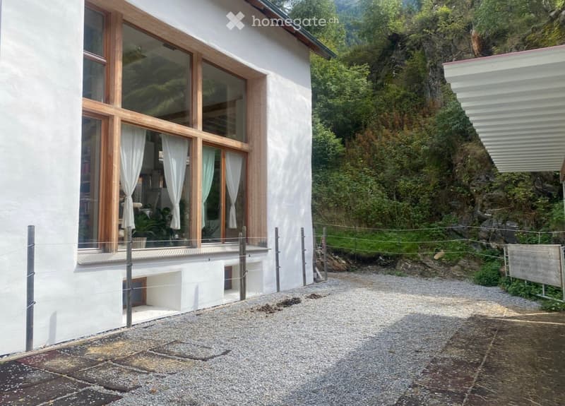 Modern white building with large wooden-framed windows and a balcony overlooking a rocky, green landscape.