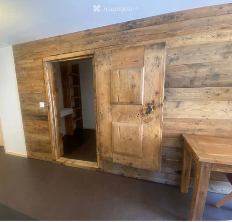 Empty room with wooden walls, a large wooden door, and a small wooden table in the corner.