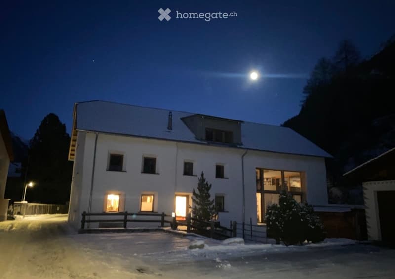 Two-story house with white exterior, illuminated windows, and snow-covered ground.