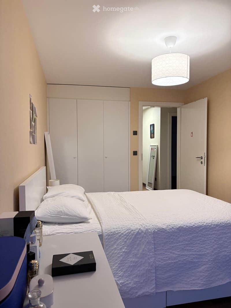 Cozy bedroom with two single beds, white bedding, a nightstand with a lamp, a wardrobe, and a mirror in the adjacent bathroom.
