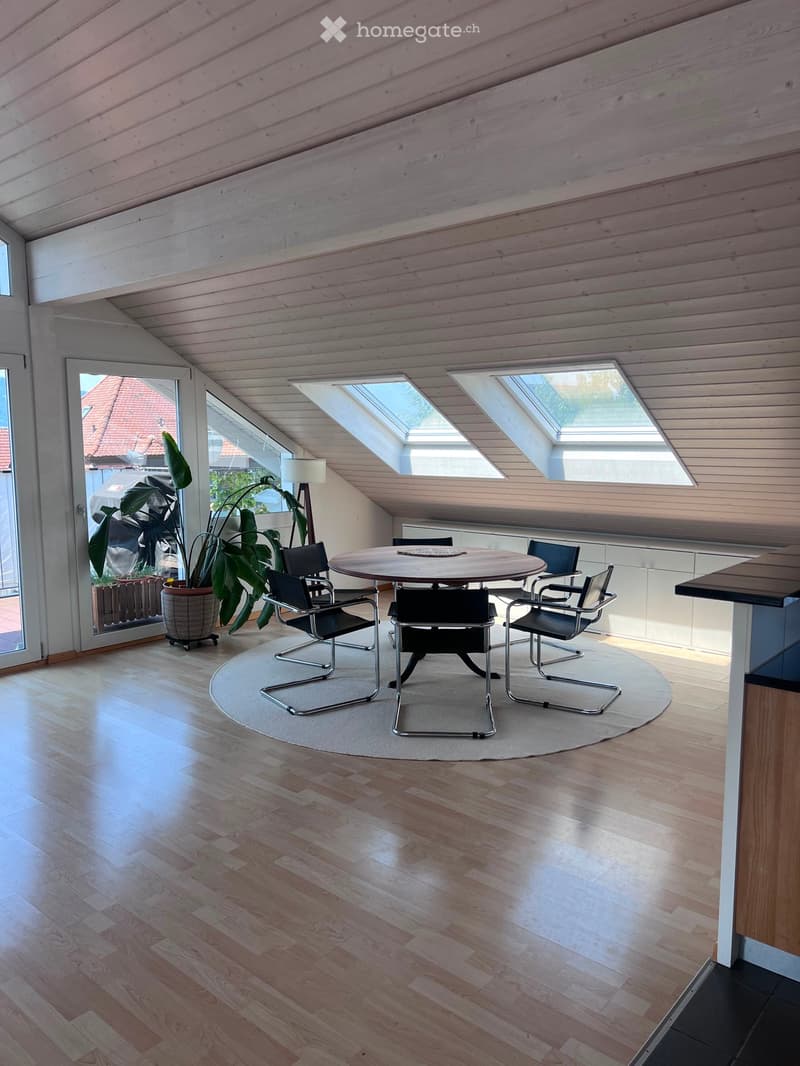 Bright, modern attic space with wooden floors, skylights, and a round dining area with chairs and a table.