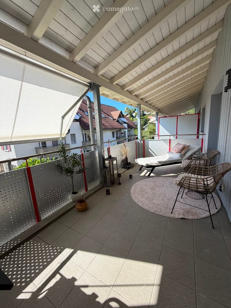 Balcony with tiled floor, white wooden ceiling, and modern furniture including a sofa, chairs, a round table, and a small plant.