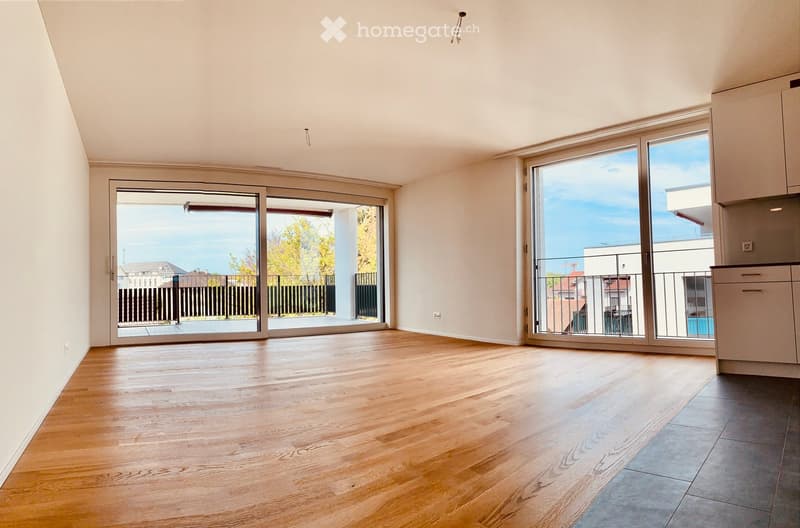 Empty room with wooden flooring, large sliding glass doors leading to a balcony, and white walls.