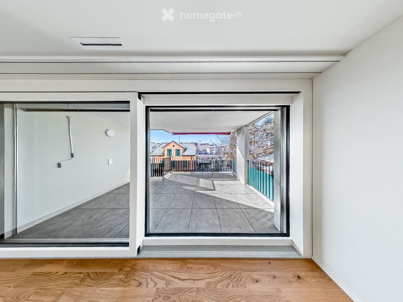 Empty room with wooden flooring, white walls, and large sliding glass doors leading to a balcony with a tiled floor and metal railing.