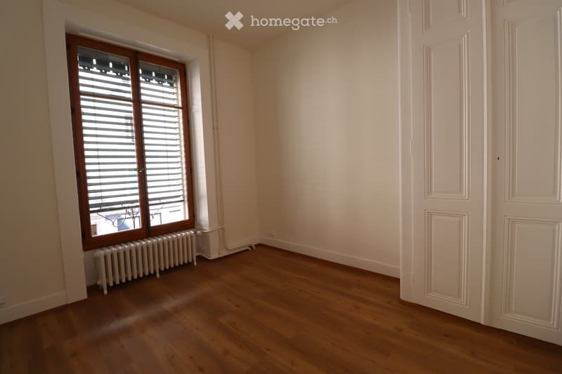 Empty room with wooden flooring, white walls, a window with blinds, and a radiator below the window.