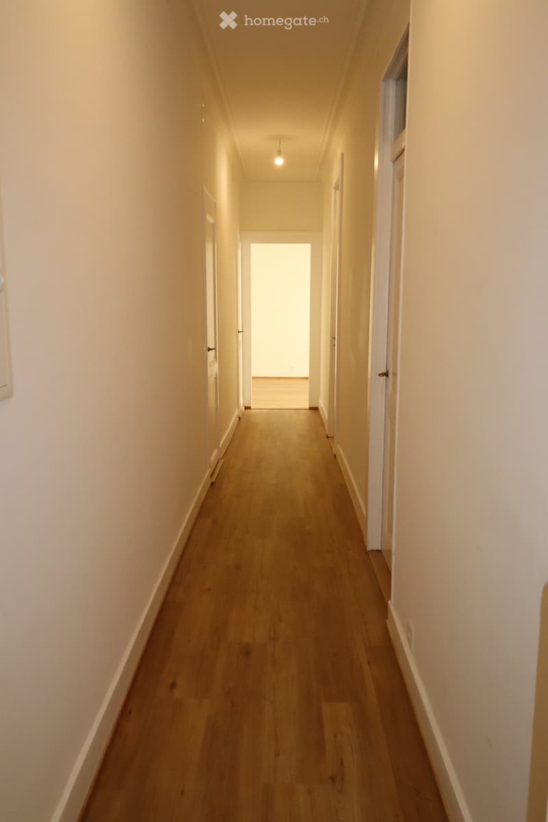 Empty hallway with wooden flooring, white walls, and several doors leading to other rooms.