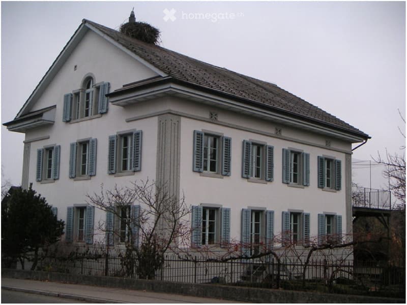 Two-story house with light pink exterior, multiple windows with shutters, and a small balcony on the right side.