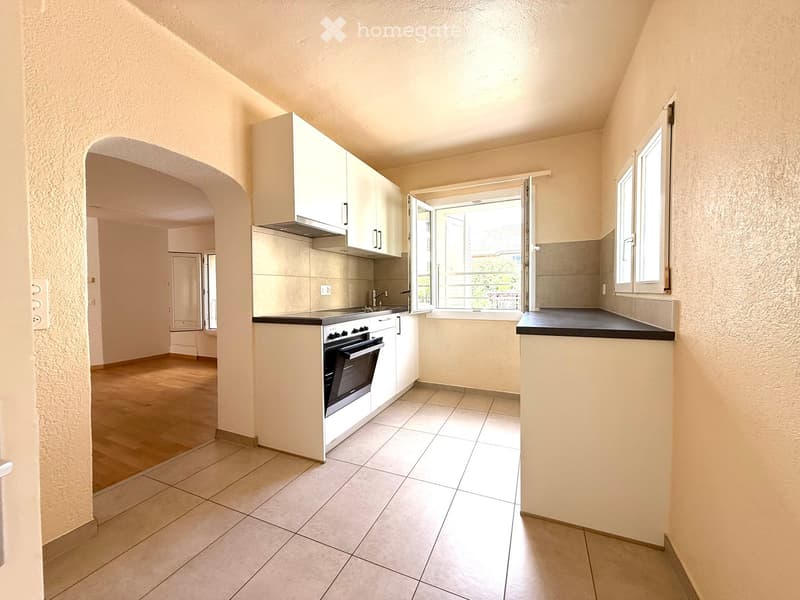 Modern kitchen with white cabinets, a built-in oven, and a sink, featuring tiled floors and large windows that let in natural light.