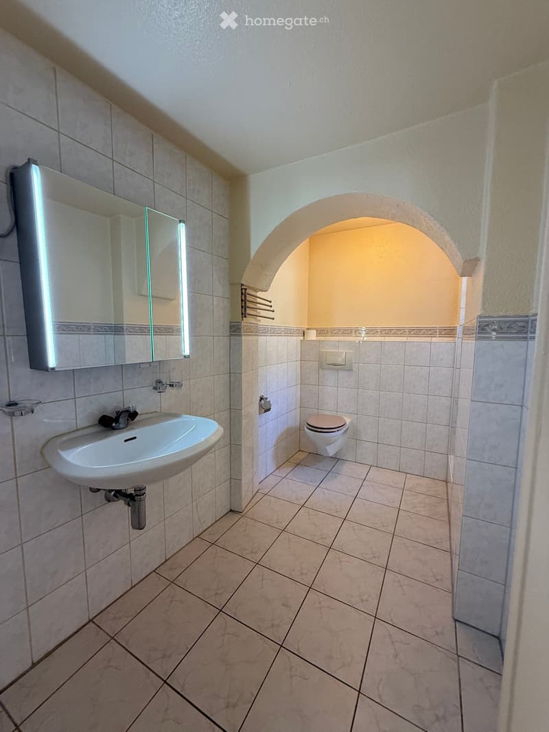 Modern bathroom with beige tiles, a white sink, a toilet, a large mirror with LED lighting, and a towel rack.