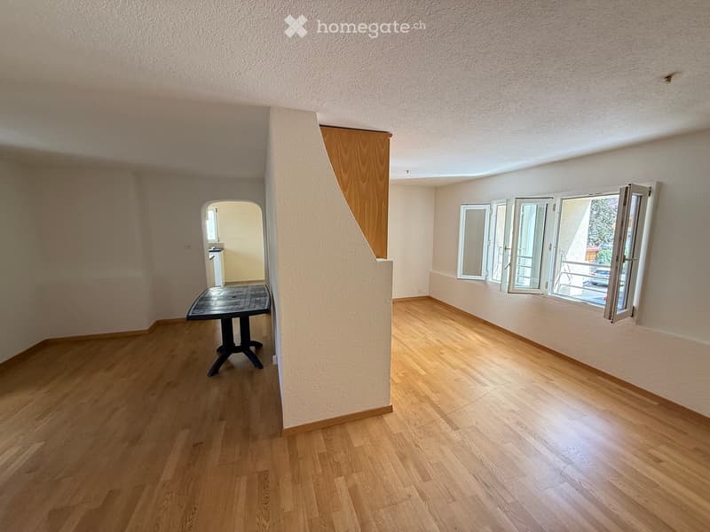 Empty room with wooden flooring, large windows, and a small table near the entrance.