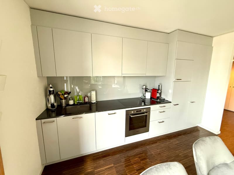 Modern kitchen with white cabinets, black countertop, stainless steel sink, oven, and coffee maker.