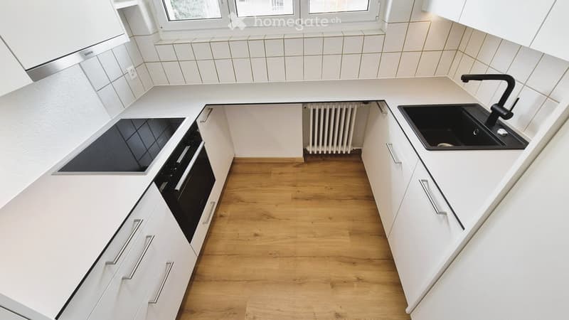 Modern kitchen with white cabinets, wooden flooring, a black sink, a faucet, and an oven.