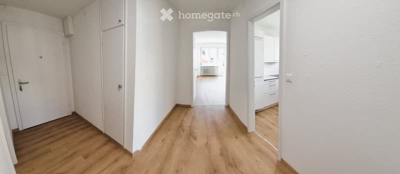 Empty hallway with wooden flooring, white walls, and doors leading to other rooms.