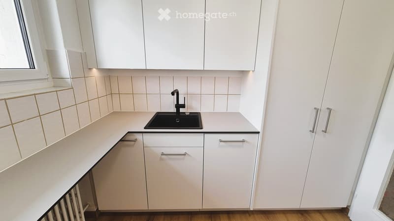 Modern kitchen with white cabinets, a black sink, and a sleek faucet. The countertops are light-colored, and the backsplash features beige tiles with a subtle pattern.