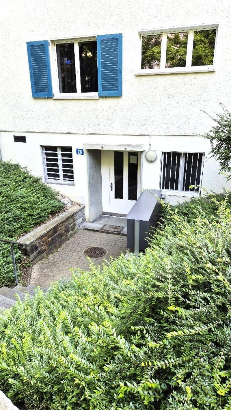 Two-story residential building with white facade, blue shutters, and a raised entrance area with steps.