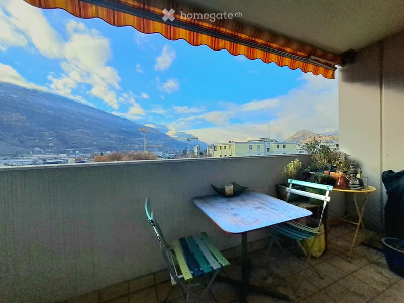 Balcony with a table, chairs, and plants, offering a scenic mountain view.