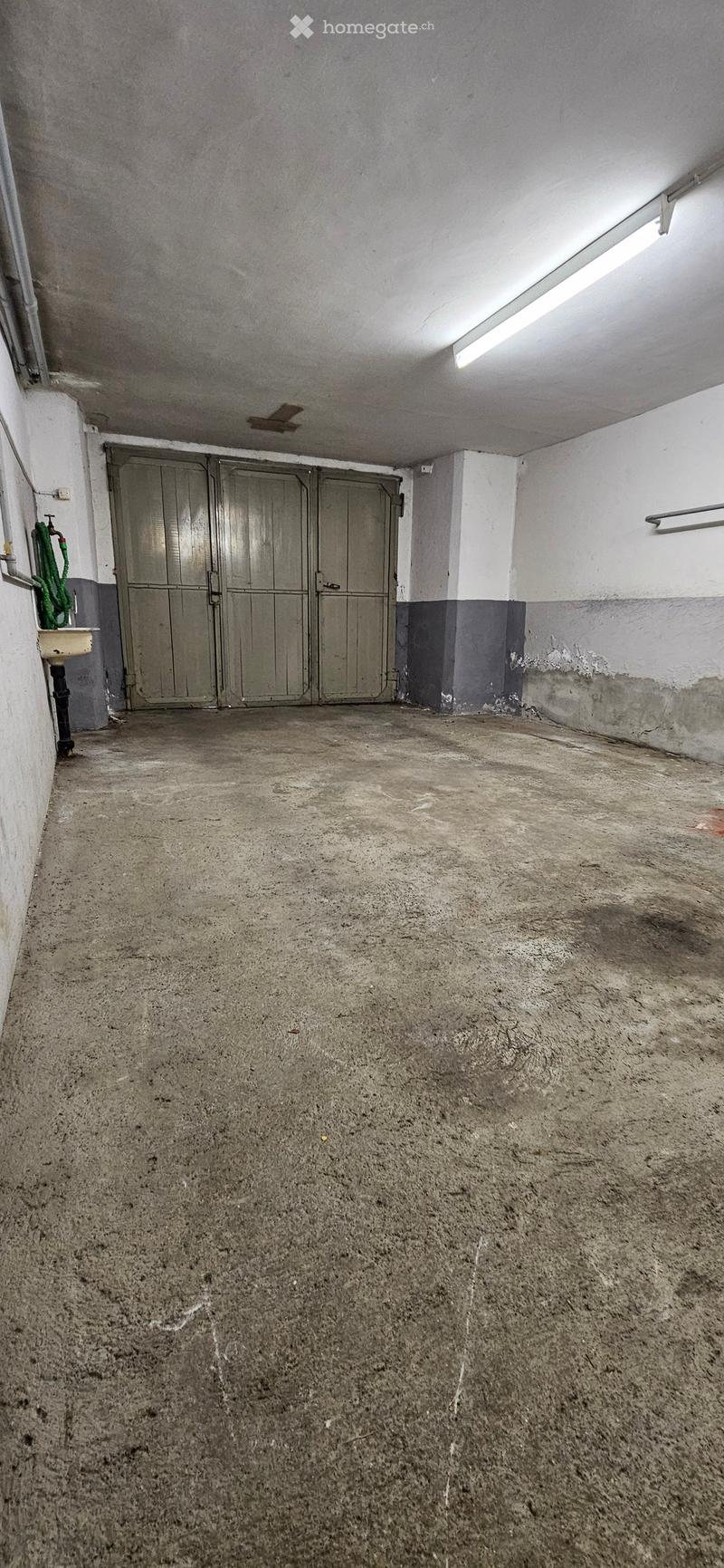 Empty garage with concrete floor, metal doors, and a small sink area on the left side.