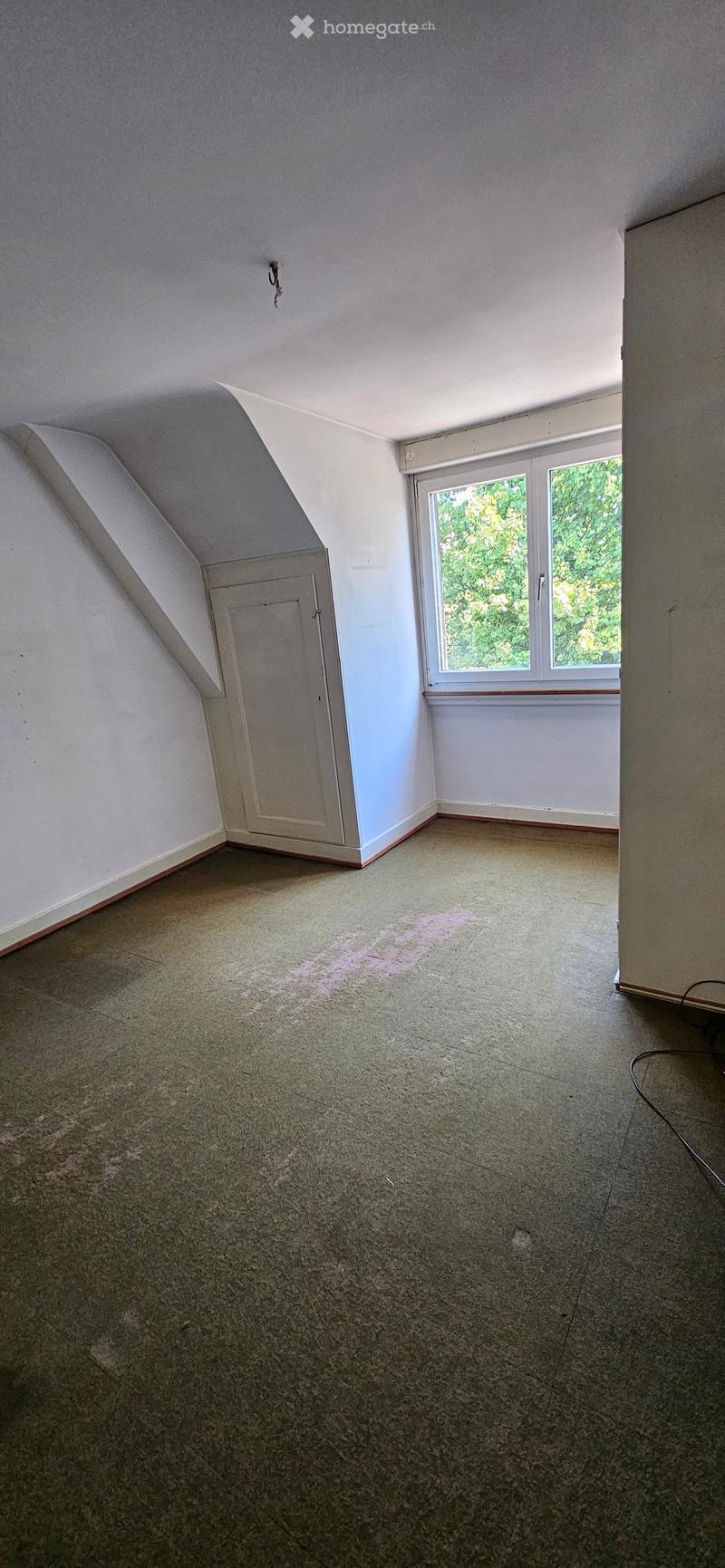 Empty attic room with sloped ceilings, carpeted floor, single window, and a small closet door.