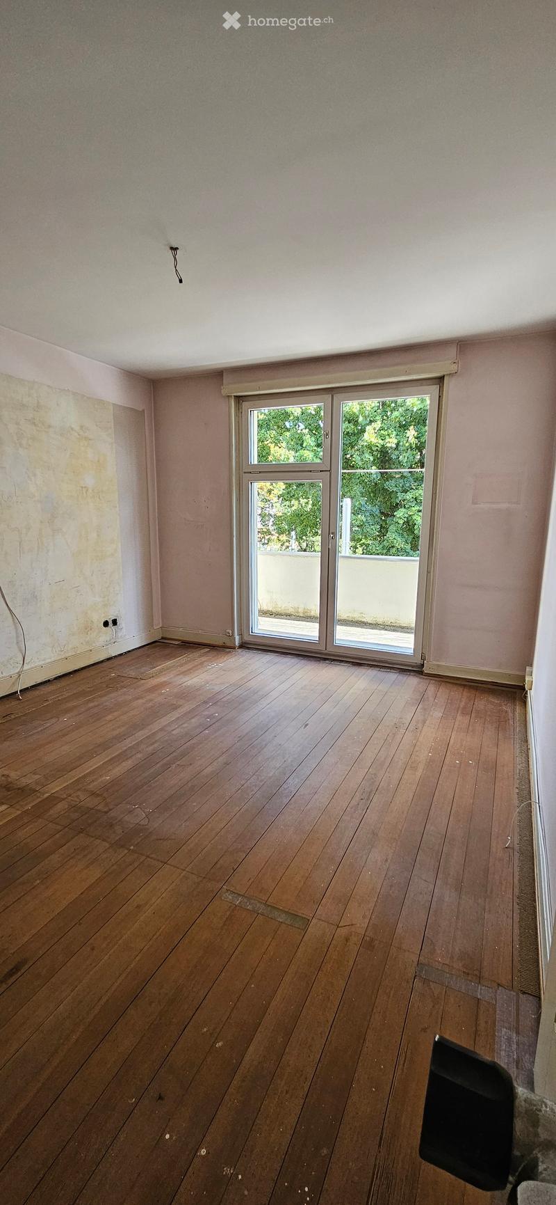 Empty room with wooden flooring, light pink walls, and a large sliding glass door leading to a balcony.