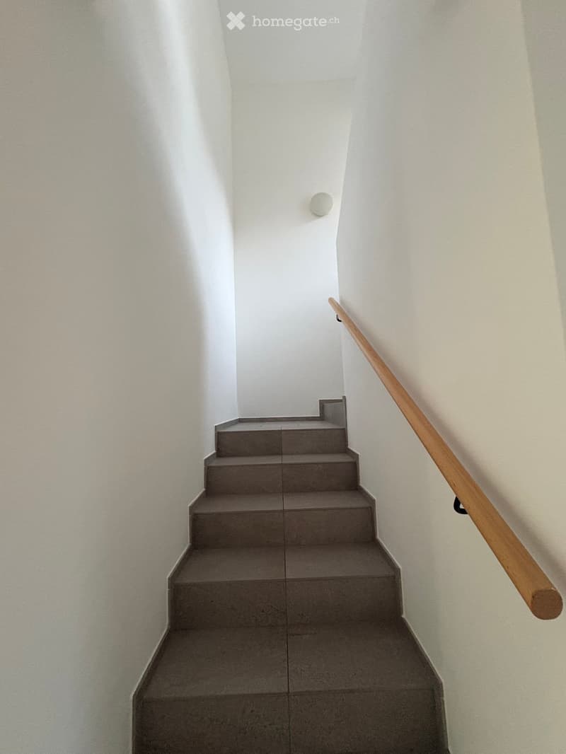 Modern staircase with grey concrete steps and a wooden handrail, set against white walls.