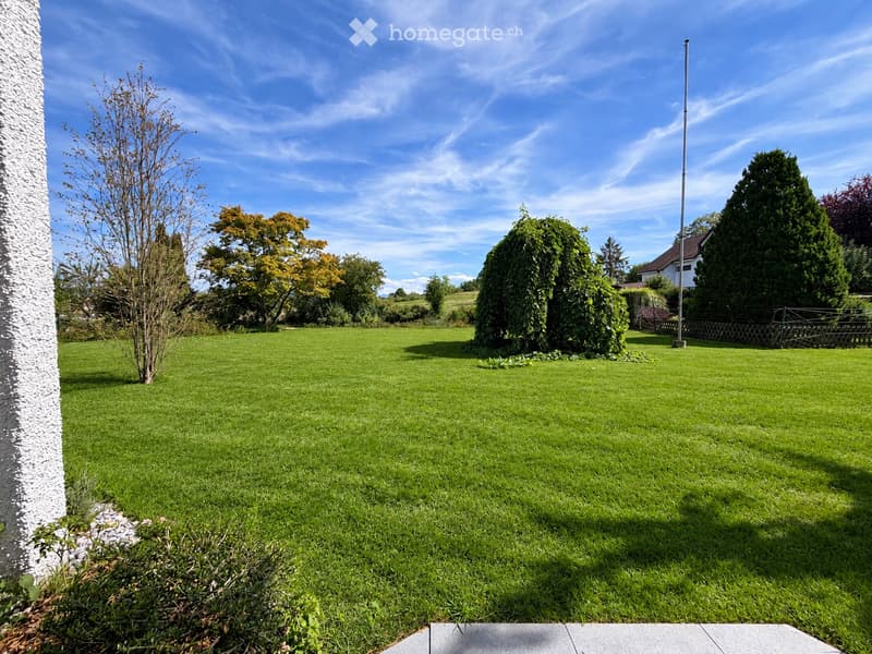 Well-maintained lawn with trimmed hedges, small trees, and a flagpole in the background.