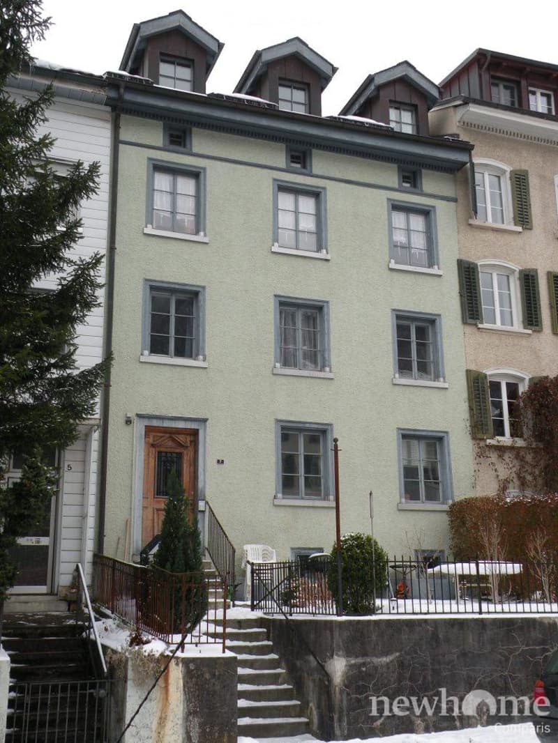 Two-story house with light green siding, multiple windows, and a raised ground floor entrance with steps.