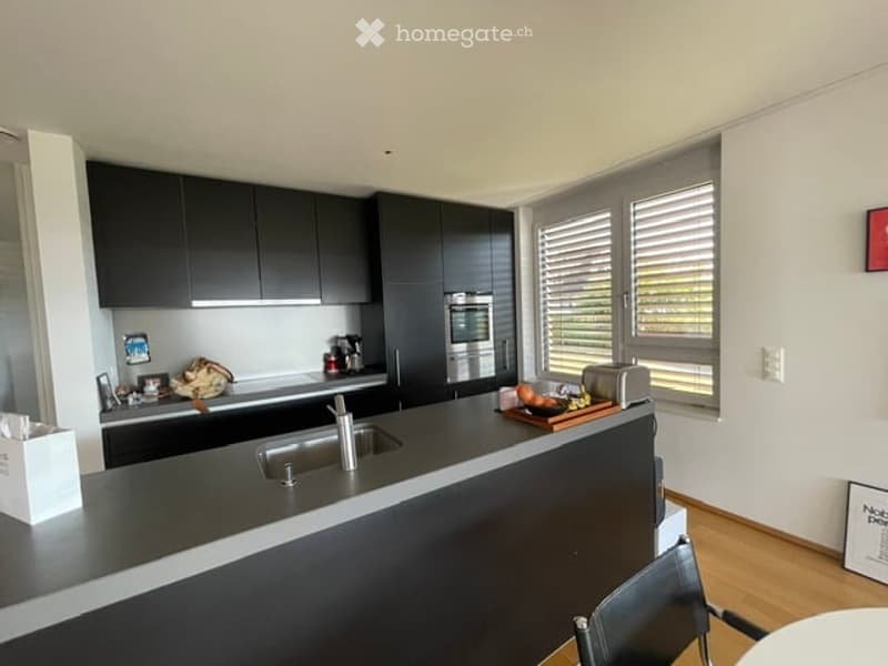 Modern kitchen with dark cabinets, stainless steel appliances, and a central island with a sink. The island features a countertop with a faucet, and there are various kitchen items including a coffee maker, toaster, and a chair near the island.